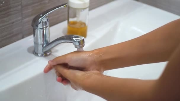 Ребенок-подросток моет руки с мылом под проточной водой в раковине, а затем выключает кран. Очистите руки, чтобы предотвратить распространение бактерий и вирусной инфекции. Защита во время пандемии. — стоковое видео