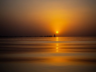 Güzel manzara manzarası. Denizde altın gün batımı. Deniz feneri manzaralı, okyanusun sakin ve sakin yüzeyi. Dalgaların üzerinde turuncu şafak güneşinin yansıması. Boşluğu kopyala.