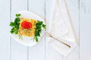 Beyaz ahşap arka planda kabak, peynir, yumurta, domates ve yeşiller. Tabakta bir porsiyon güveç. Sağlıklı bir kahvaltı. Zayıflık ve kilo kaybı için nefis bir diyet yemeği. Üst görünüm düzlüğü