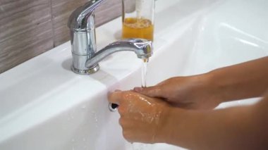 Genç bir çocuk lavaboda akan suyun altında ellerini sabunla yıkıyor ve sonra musluğu kapatıyor. Bakteri ve virüs bulaşmasını önlemek için ellerinizi temizleyin. Bir salgın sırasında koruma.