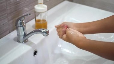 Genç bir çocuk lavaboda akan suyun altında ellerini tamamen sabunla yıkıyor. Bakteri ve viral enfeksiyonun yayılmasını önlemek için ellerinizi temizleyin. Bir salgın sırasında çocukları korumak.
