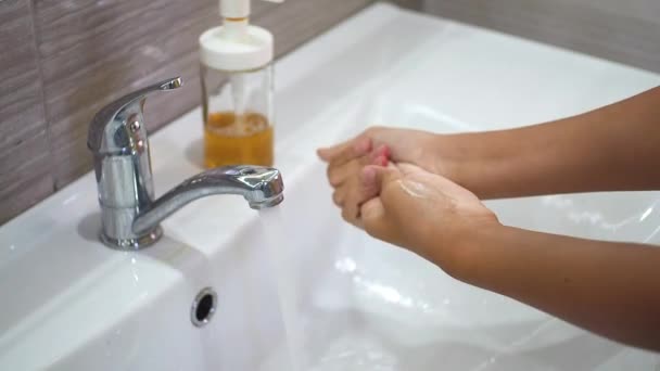 A teenage child washes his hands thoroughly with soap under running water in the sink. Clean your hands to prevent the spread of bacteria and viral infection. Protecting children during a pandemic. — Stock Video