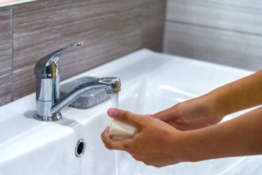 Genç bir kız ellerini lavabodaki bir su deresinin altında sabun köpüğüyle yıkıyor. Bakteri ve viral enfeksiyonun yayılmasını önlemek için temiz eller. Salgın sırasında korunma. Temizlik ve temizlik..