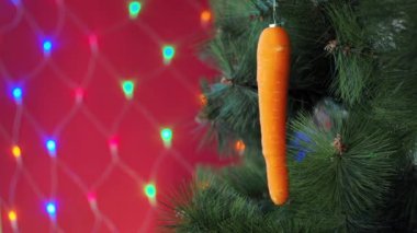 Vejetaryen Noel konseri. Ağaç taze sebzelerle süslenir. Kırmızı arka planda, çam dalında çiğ havuç ve bokeh. Minimalizm ve çevre dostu ziyan olmadan kutlama fikri. Boşluğu kopyala