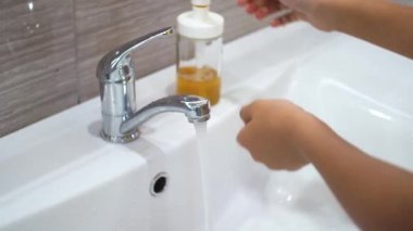 Genç bir çocuk musluğu açar ve lavaboda akan suyun altında ellerini sabunla yıkar. Bakteri ve viral enfeksiyonun yayılmasını önlemek için ellerinizi temizleyin. Bir salgın sırasında çocukları korumak.