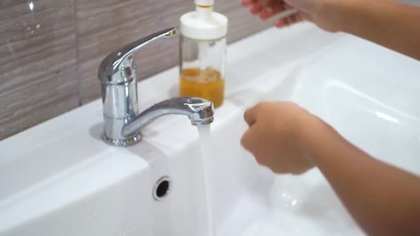 Un adolescente apre il rubinetto e si lava le mani con il sapone sotto l'acqua corrente nel lavandino. Pulisci le mani per prevenire la diffusione di batteri e infezioni virali. Proteggere i bambini durante una pandemia. — Video Stock