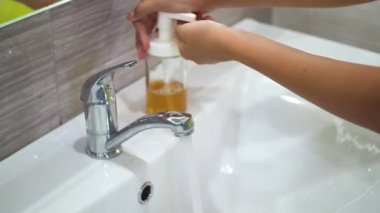 Genç bir çocuk lavaboda akan suyun altında ellerini tamamen sabunla yıkıyor. Bakteri ve viral enfeksiyonun yayılmasını önlemek için ellerinizi temizleyin. Bir salgın sırasında çocukları korumak.