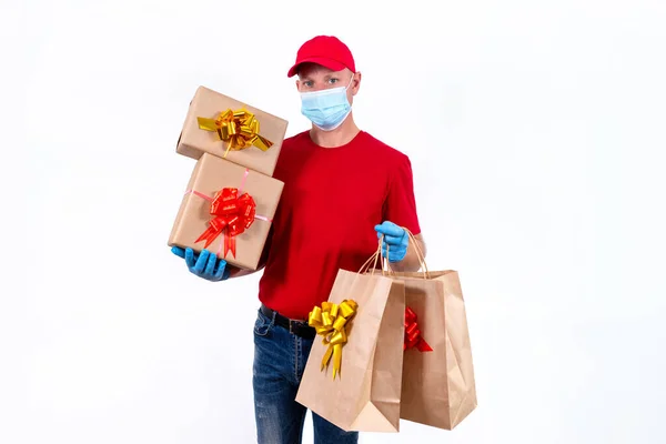 Livraison à distance sans contact de cadeaux de Noël en cas de pandémie de coronavirus. Un messager en uniforme rouge et un masque médical de protection et des gants tient un grand ordre, de nombreuses boîtes-cadeaux et des sacs avec des arcs. — Photo