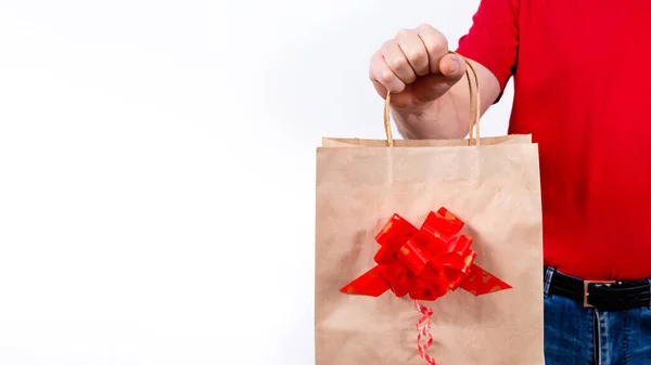 Bannière. Livraison à distance sécurisée et sans contact de cadeaux de Noël pendant la pandémie de coronavirus. Ferme là. Une main de courrier tient un sac-cadeau en papier avec arc sur un fond blanc isolé. Espace de copie. — Photo