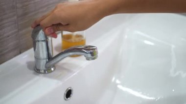 Genç bir çocuk musluğu açar ve lavaboda akan suyun altında ellerini sabunla yıkar. Bakteri ve viral enfeksiyonun yayılmasını önlemek için ellerinizi temizleyin. Bir salgın sırasında çocukları korumak.