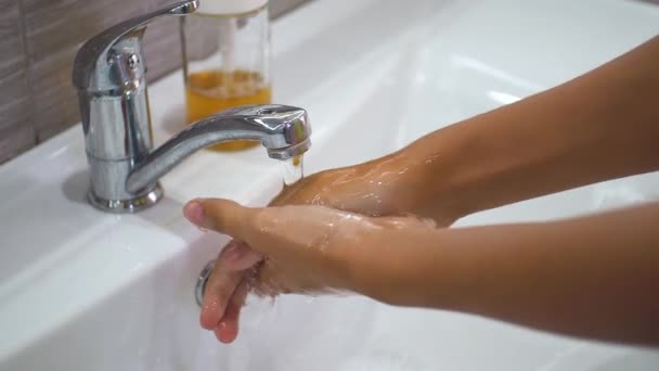 Ein Teenager wäscht sich im Waschbecken unter fließendem Wasser die Hände mit Seife und dreht dann den Wasserhahn zu. Reinigen Sie Ihre Hände, um die Ausbreitung von Bakterien und Virusinfektionen zu verhindern. Schutz während einer Pandemie. — Stockvideo