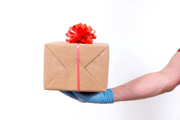 Veilige contactloze levering op afstand van vakantiegeschenken tijdens de coronavirus pandemie. Sluit maar af. Courier hand in beschermende medische handschoenen houdt een mooie geschenkdoos met een strik op een witte achtergrond. — Stockfoto