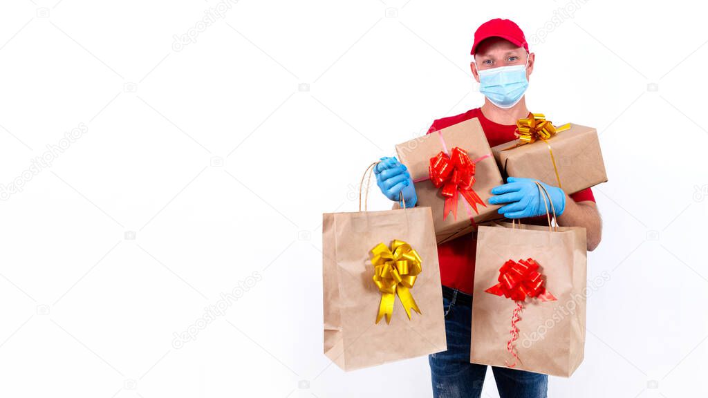 Safe contactless remote delivery of holiday gifts during coronavirus pandemic. A courier in red uniform and protective medical mask and gloves holds large order, many gift boxes and bags with bows.