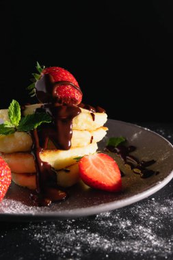 Koyu arkaplanlı, piramitli ve sıvı çikolata ve çilekle süslenmiş peynirli kekler..