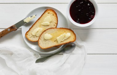 Beyaz bir tabakta tereyağlı iki çıtır tost bıçağın yanında ve beyaz ahşap arka planda reçel..
