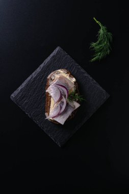 Ringa balığı dilimli çavdar ekmeği kanepeleri, koyu arkaplanda dereotu ve kırmızı soğan. Seçici odak