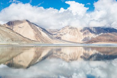 Pagong Gölü üzerinde beyaz bulutlu ve mavi gökyüzü olan yüksek dağın yansımaları, Leh Ladakh, Hindistan.