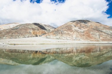 Pagong Gölü üzerinde beyaz bulutlu ve mavi gökyüzü olan yüksek bir dağın yansımaları, Leh Ladakh, Hindistan.