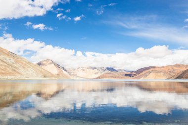 Pagong Gölü üzerinde beyaz bulutlu ve mavi gökyüzü olan yüksek bir dağın yansımaları, Leh Ladakh, Hindistan.