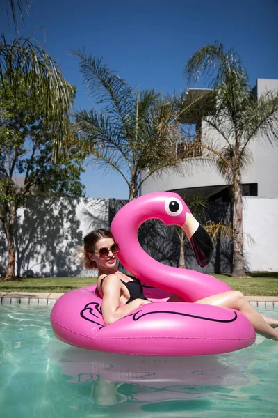 Kız güneşli bir günde havuzda şişme pembe bir flamingoda yüzmekten hoşlanıyor..