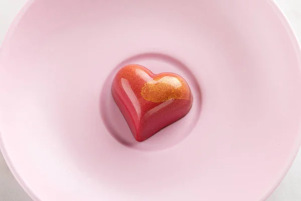 Red heart shaped handmade chocolate candy on pink plate. Exclusive handcrafted bonbon. Luxury exclusive chocolates for Valentines Day