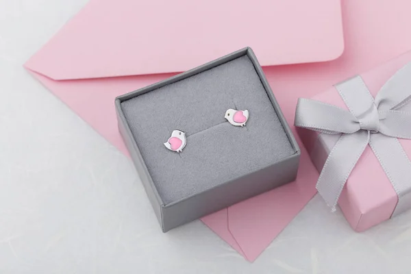 Bird shape with heart earring studs in gray gift box on pink envelope background. Cute jewelry for child girl. Present for birthday