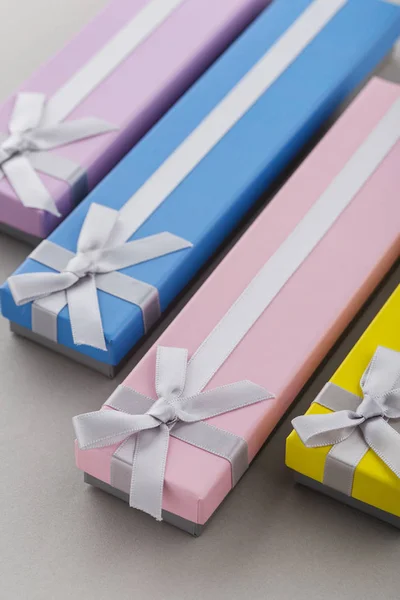 Colorful present boxes with ribbon bows on gray background. Pink, yellow, blue and violet long gift boxes for holiday presents