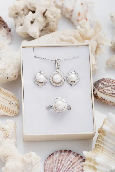 Jewelry set of elegant silver earrings, ring and pendant necklace with pearl and diamonds in gift box on coral. Luxury jewelry on natural textured background