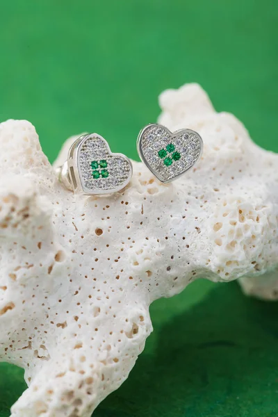 Luxury heart stud earrings with crystals on coral against green background. Silver bridesmaid jewelry with diamonds. Summer beach wedding concept