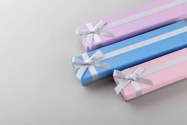 Three colorful gift boxes with ribbon bows on gray background. Blue, pink and violet long boxes. Presents for holidays
