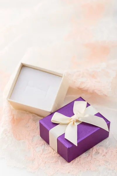 Small purple jewelry gift box with bow on lace background. Paper present box for ring
