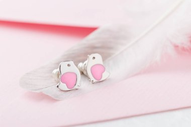 Kuş şekli kalp küpe Çıtçıt üzerinde tüy ile pembe arka plan ile. Kız çocuk için sevimli takı. Doğum günü için hediye