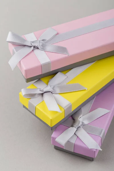 Colorful gift boxes with ribbon bows on gray background. Pink, yellow and violet long boxes. Presents for holidays