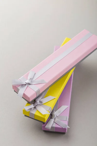 Colorful gift boxes with ribbon bows on gray background. Pink, yellow and violet long boxes. Presents for holidays