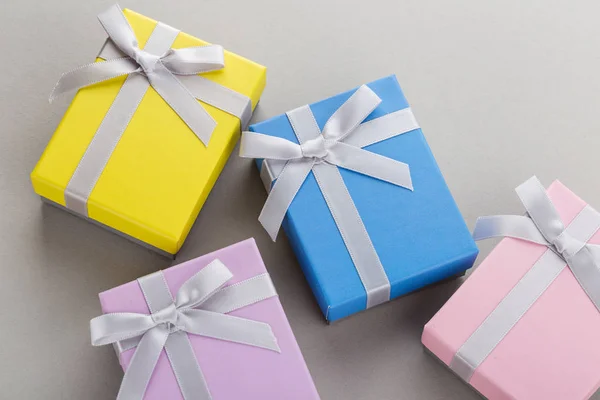 Small colorful gift boxes with ribbon bows on gray background. Pink, yellow, blue and violet boxes for for jewelry or holiday presents