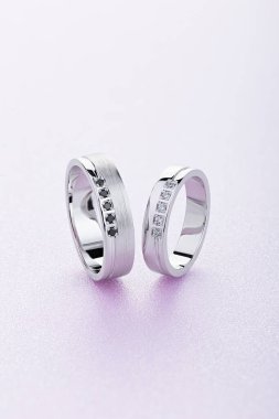 Pembe arka planda elmasları olan bir çift beyaz altın alyans. Siyah ve beyaz değerli taşlı orijinal gümüş alyans. Mücevher reklamı hala hayat dolu