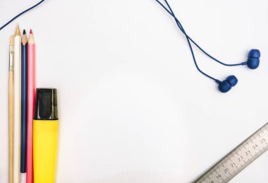 Kalemler, kalemler, kulaklıklar ve bir cetvel beyaz bir kağıt üzerinde.