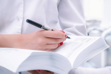 Tıp çalışanı, doktor ya da hemşire elinde tükenmez kalemle elinde büyük bir referans defteri tutuyor.