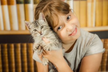 Gri çizgili kedi yavrusunu kucaklayan mutlu ve gülümseyen bir kız.