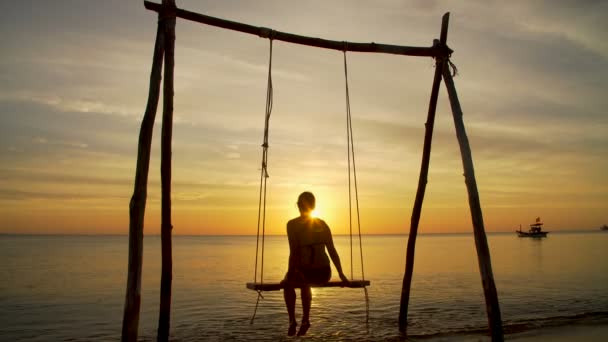 Chica en un columpio en la orilla del mar en la puesta del sol — Vídeos de Stock