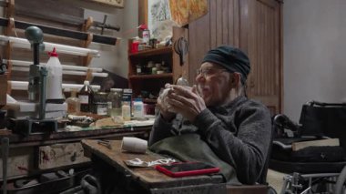 Tekerlekli sandalyedeki yaşlı erkek usta atölyesinde mobilyaları restore ediyor.