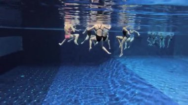 Senkronize yüzme takımı yüzme havuzunda, su altında antrenman yapıyor.
