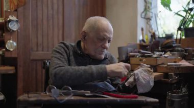 Senior gray haired male master in a wheelchair is working at his workshop sharpening japanese swords blade