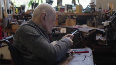 Senior gray haired male master in a wheelchair is working at his workshop sharpening japanese swords blade