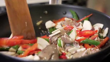 Chef is frying chopped chicken liver with vegetables and mushrooms in a pan