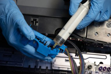 Bir yazıcıdan mürekkep emmek için elektrikli süpürge kullanan bir teknisyenin üst görüntüsü.