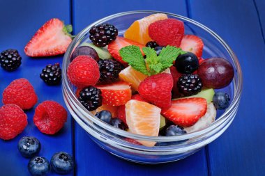 Mavi ahşap masa üzerinde bir kasede sağlıklı taze meyve salatası