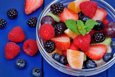 Mavi ahşap masa üzerinde şeffaf bir kase çilek salatası