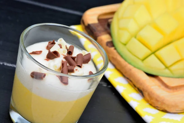 Mousse di frutta al mango con panna montata e cioccolato in un barattolo di vetro su un tavolo di legno — Foto Stock