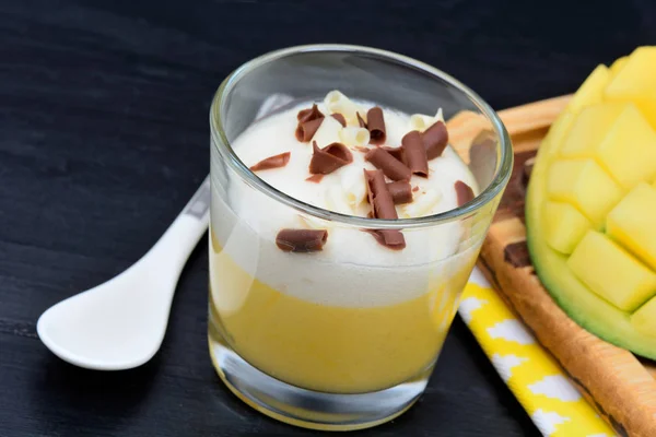 Mousse di mango con cioccolato in un bicchiere e cubetti di mango su un tavolo di legno — Foto Stock
